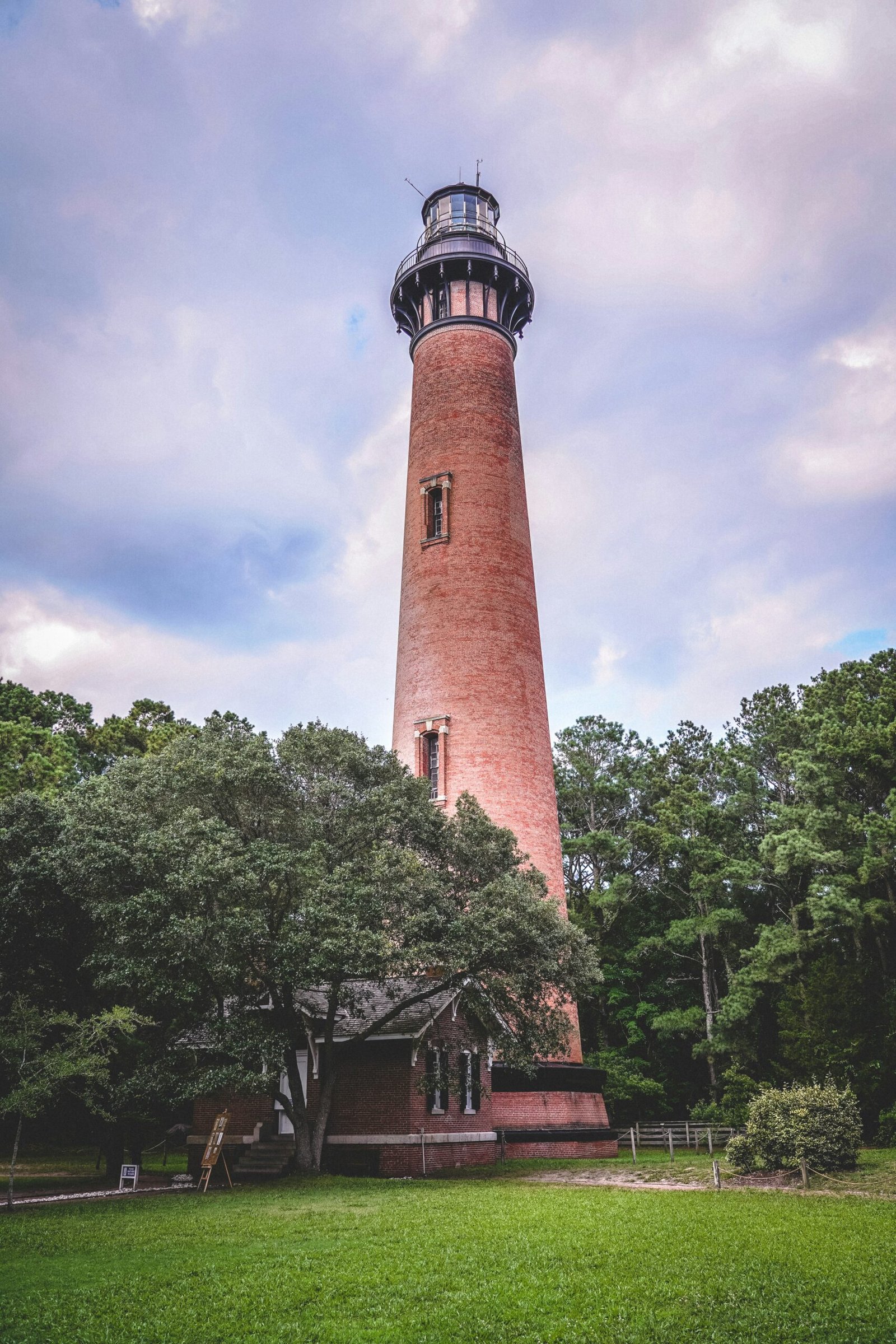 brown and black concrete lighthouse near green trees under white clouds and blue sky during daytime